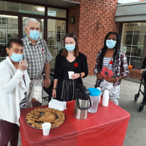 students at retirement complex on remembrance day. standing behind table of cookies with a resisdent. 